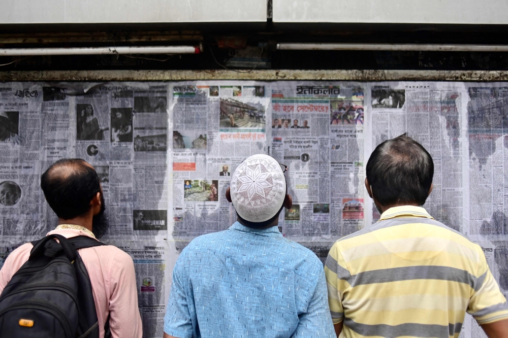 In this photograph taken on September 1, 2023, pedestrians read Bangladesh's local newspapers displayed along a street in Dhaka. (Photo by Munir Uz Zaman / AFP) /