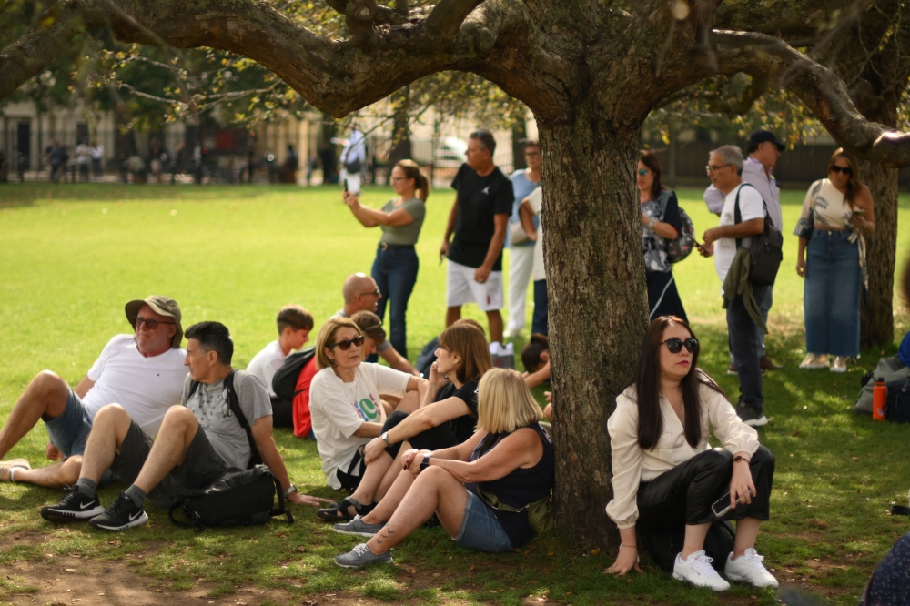 People take shelter from the sun in the shade of a tree in central London on September 8, 2023 as the late summer heatwave continues. (Photo by Daniel Leal / AFP)

