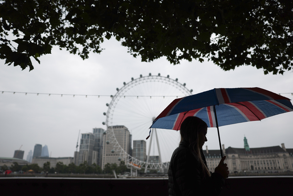 Pedestrians shelter from the rain beneath umbrellas while walking past the London landmark, the London Eye, from Embankment by the River Thames, in central London, on August 18, 2023 on a gloomy summer's day. Photo by HENRY NICHOLLS / AFP

