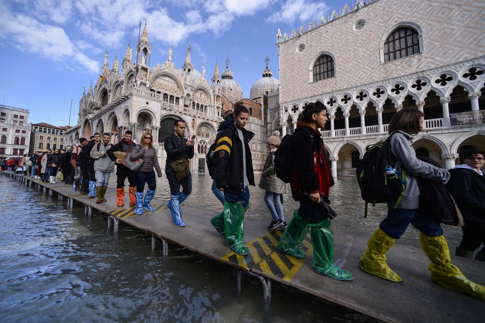 People walk on a footbridge across the flooded St. Mark's Square by St. Mark's Basilica (rear) and the Doge's palace (right) on November 14, 2019 in Venice. (Photo by Filippo Monteforte / AFP)