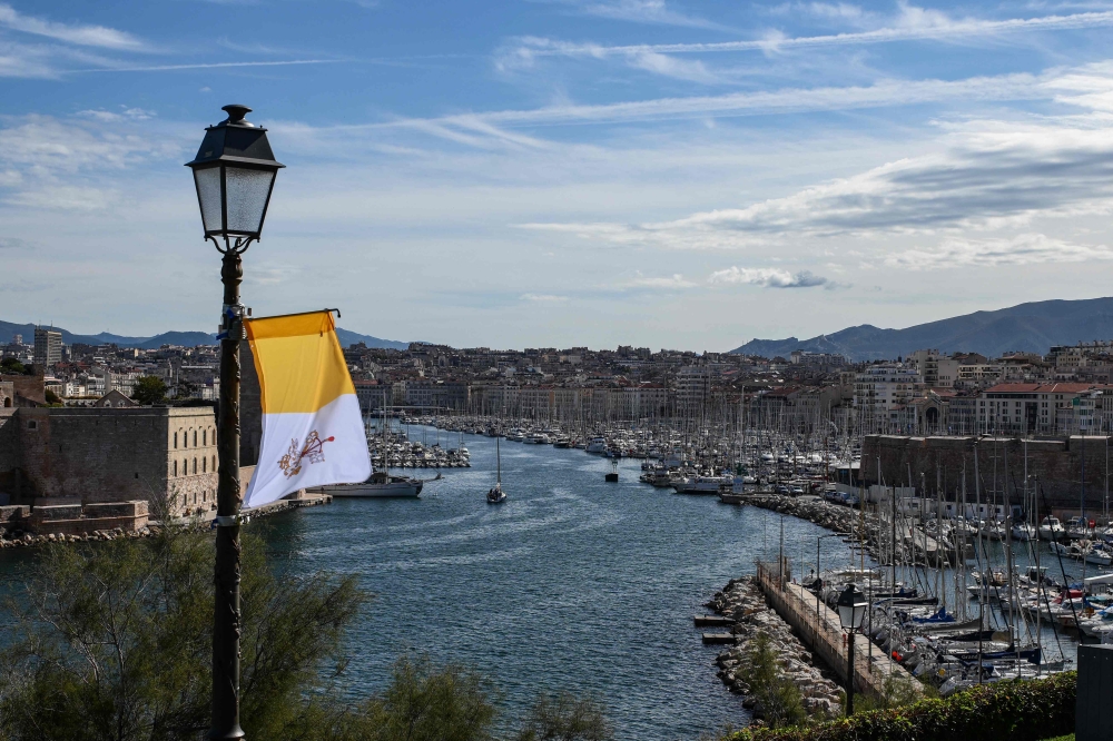 :This photograph taken on September 22, 2023, shows a view of the Old Port (R) of Marseille and of the Saint-Jean Fort, with a Vatican flag held on a lamp post, prior to the Pope's visit to the city. Pope Francis heads to Marseille for a two-day visit focused on the Mediterranean and migration, bringing a message of tolerance amid bitter debate over how Europe manages asylum seekers. (Photo by CHRISTOPHE SIMON / AFP)
