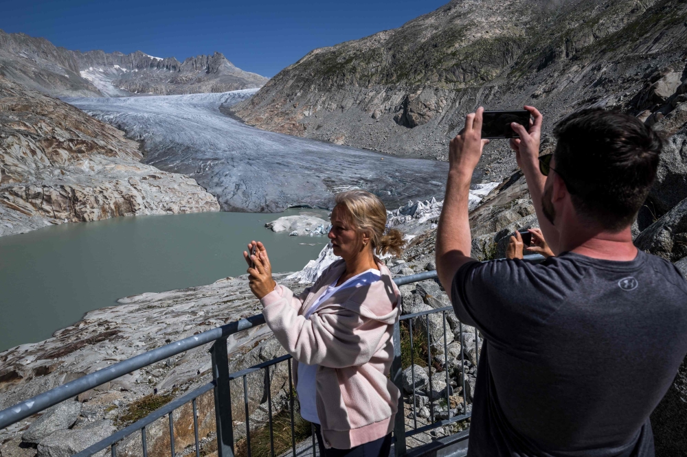 (Files) A photograph taken on August 24, 2023 above Gletsch, in the Swiss Alps shows tourists taking a picture of the Rhone Glacier and its glacial lake due to the melting of the glacier. (Photo by Fabrice Coffrini / AFP)
 