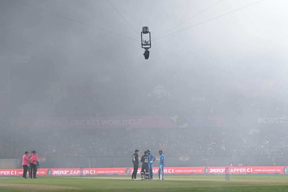 India's Virat Kohli (right) along with other players looks on as fog hovers over the field during the 2023 ICC Men's Cricket World Cup one-day international (ODI) match between India and New Zealand at the Himachal Pradesh Cricket Association Stadium in Dharamsala on October 22, 2023. (Photo by Money Sharma / AFP)