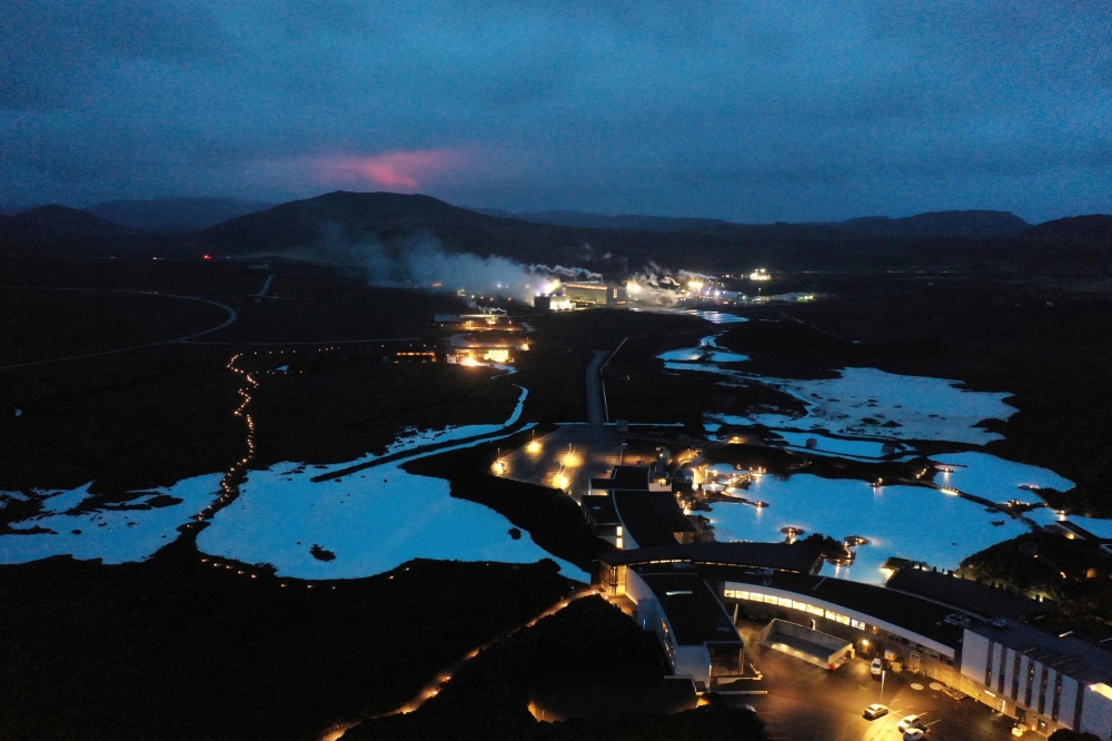 The red shimmer from magma is seen coming out from the erupting Fagradalsfjall volcano behind the tourist land mark Blue Lagoon, near the town of Grindavik some 40 km west of the Icelandic capital Reykjavik, on March 20, 2021. Photo by Halldor KOLBEINS / AFP