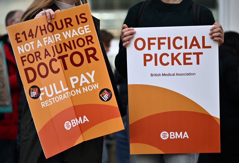 People hold British Medical Association (BMA) branded placards calling for better pay, as they stand on a picket line outside University College Hospital (UCH) in central London on April 12, 2023, during a strike by junior doctors -- physicians who are not senior specialists but who may still years of experience. Photo by Ben Stansall / AFP