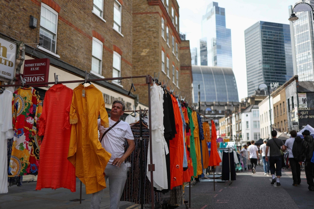 Shoppers browse stalls in Petticoat Lane Market, against the backdrop of The City of London financial district in London on August 11, 2023.  Photo by HENRY NICHOLLS / AFP
