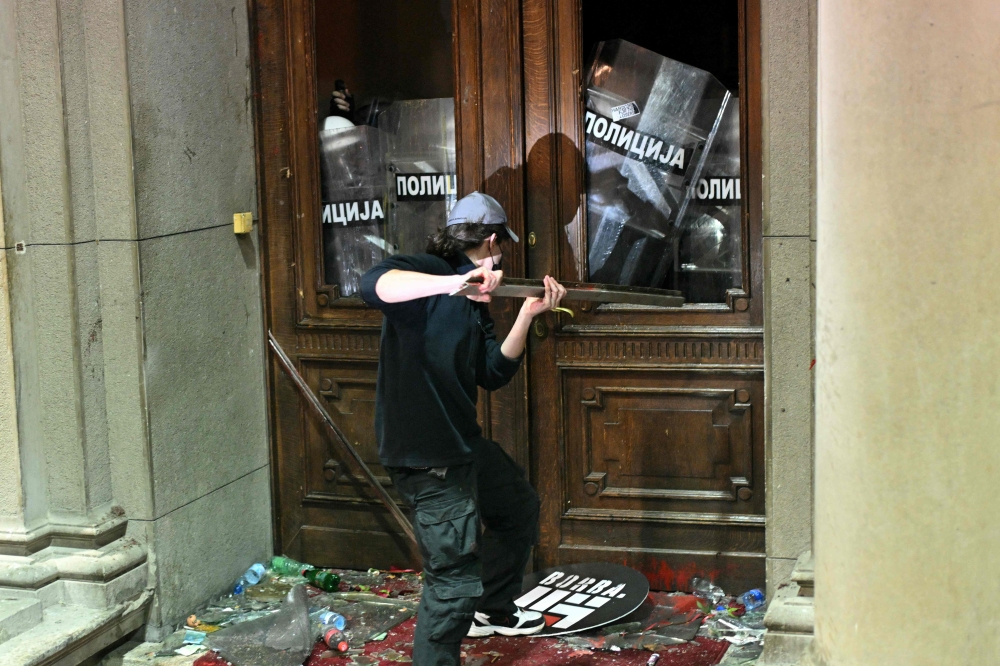 A protester uses a metal object against police officers guarding the entrance to the Belgrade's city council building during a demonstration in Belgrade, on December 24, 2023. (Photo by Oliver Bunic / AFP)