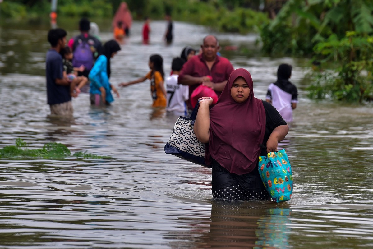 A woman carries her belongings as she walks through floodwaters following heavy rain in Thailand's southern province of Narathiwat on December 25, 2023. Photo by Madaree TOHLALA / AFP