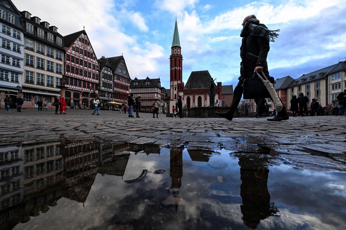 A pedestrian is reflected in a puddle as he walks at the Roemerplatz, the city's central square in Frankfurt am Main, western Germany, on January 3, 2024. Photo by Kirill KUDRYAVTSEV / AFP