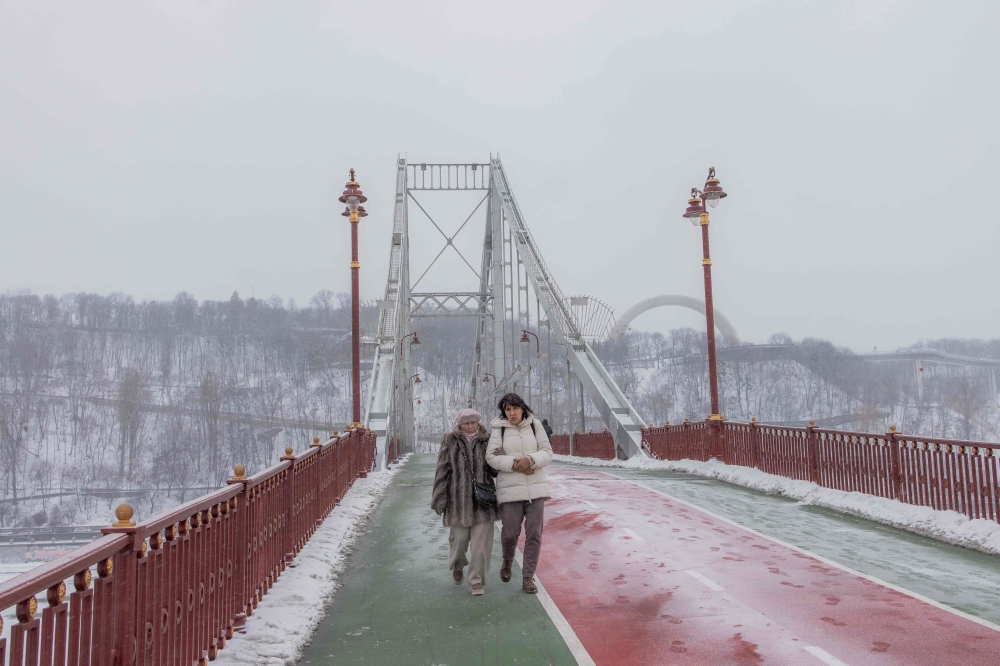 Local residents walk on a bridge over the Dnipro River in Kyiv, on January 14, 2024, amid the Russian invasion of Ukraine. (Photo by Roman PILIPEY / AFP)