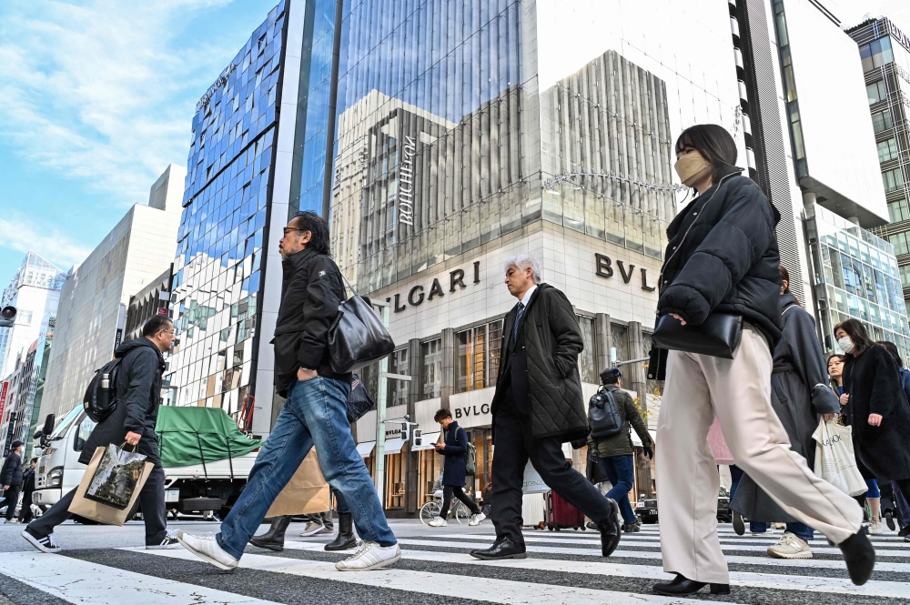 Pedestrians cross the street in front of luxury shops at the Ginza shopping district in Tokyo on January 19, 2024. Photo by Richard A. Brooks / AFP