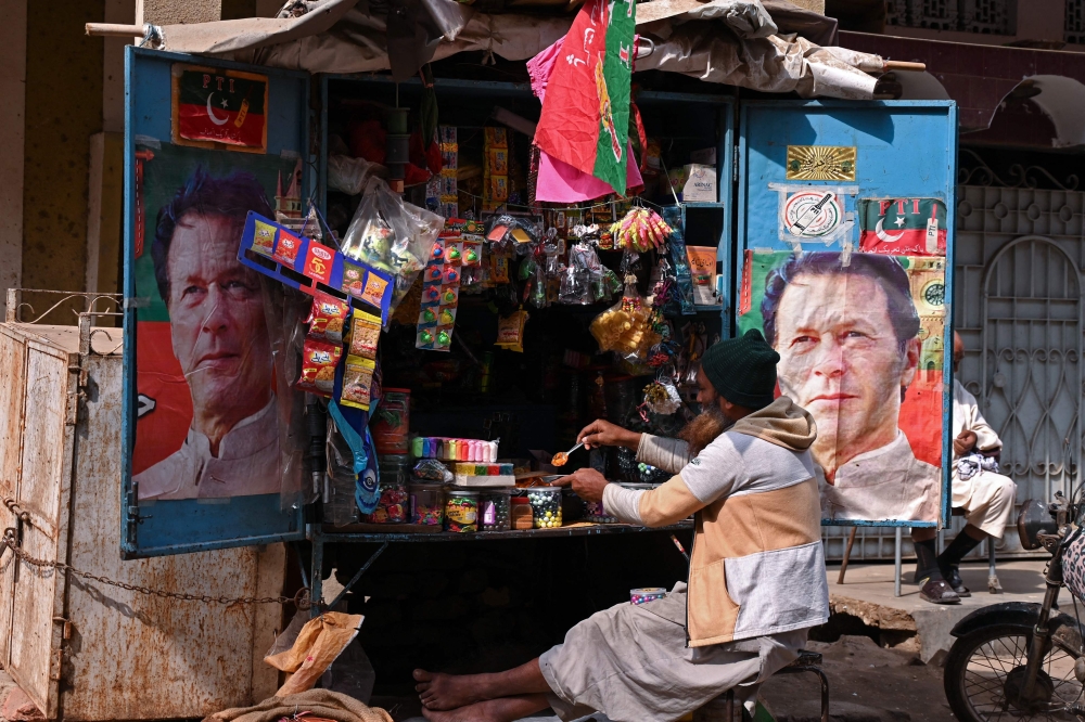 A vendor sits at his tuck shop displaying posters of Pakistan's former Prime Minister and Pakistan Tehreek-e-Insaf (PTI) leader Imran Khan, in Hyderabad on January 29, 2024. (Photo by Akram SHAHID / AFP)
 