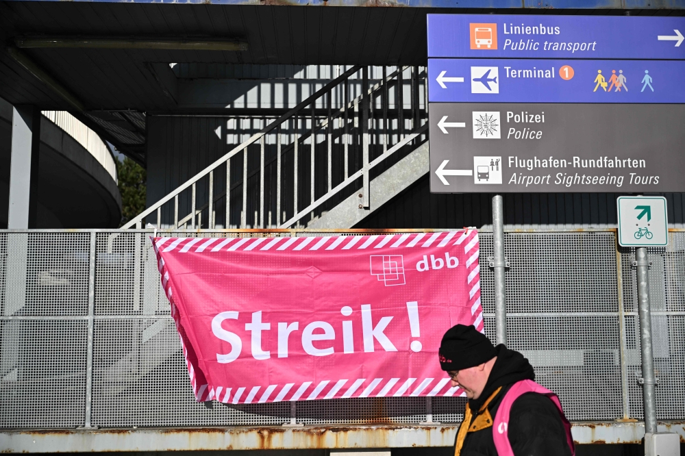 A participant walks past a banner of the German Civil Service Association (dbb beamtenbund und tarifunion) outside a terminal at Frankfurt Airport, Frankfurt am Main, western Germany on February 1, 2024, as flights are cancelled or delayed due to a nationwide strike of airport security staff. Photo by Kirill KUDRYAVTSEV / AFP