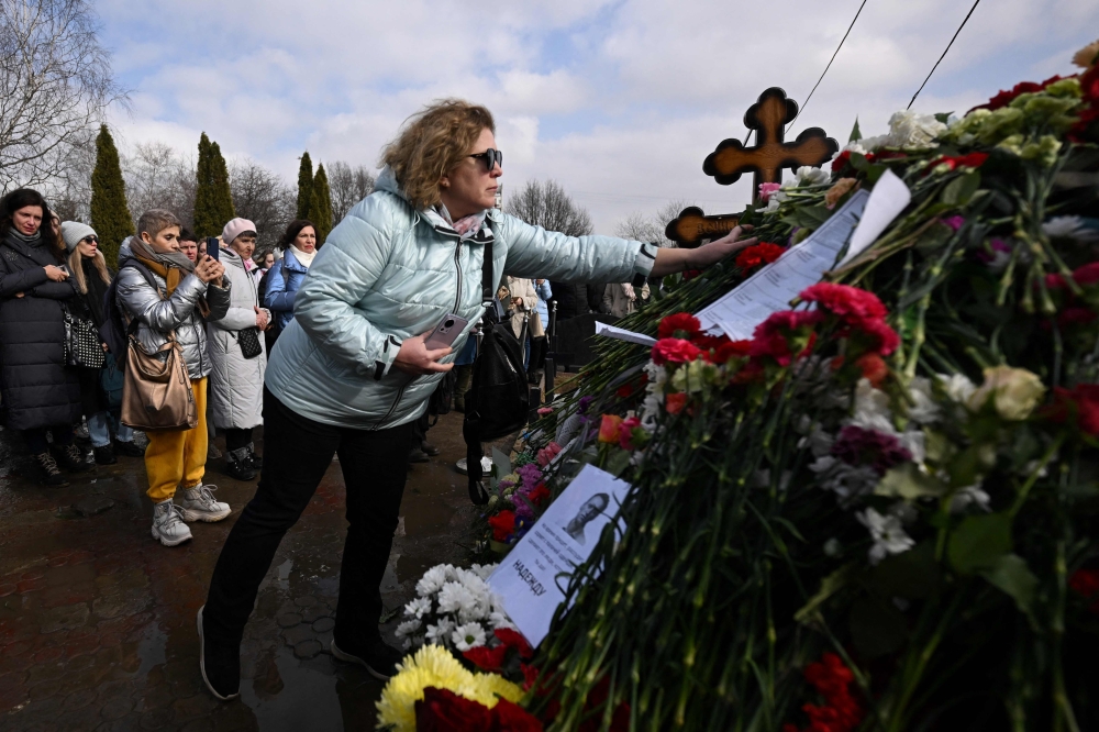 A woman lays flowers at the grave of late Russian opposition leader Alexei Navalny on the day of Russia's presidential election in Moscow on March 17, 2024. Photo Credit: NATALIA KOLESNIKOVA / AFP. 