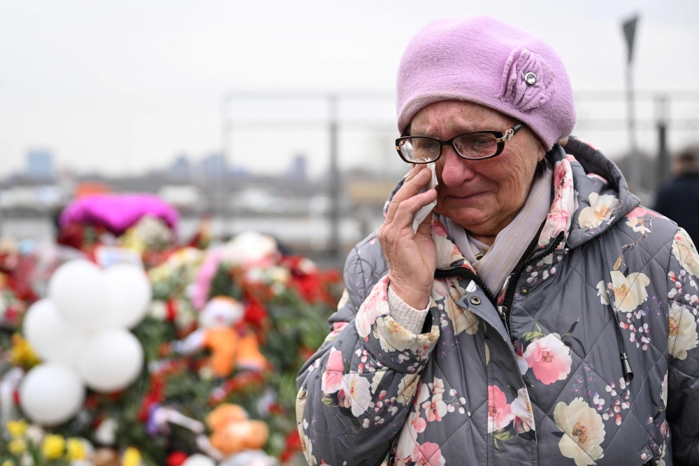 A woman reacts as she stands at a makeshift memorial in front of the Crocus City Hall in Moscow's northern suburb of Krasnogorsk on March 29, 2024, a week after a deadly attack by gunmen on a Moscow concert hall killed at least 143 people and wounded dozens more. (Photo by Natalia Kolesnikova / AFP)