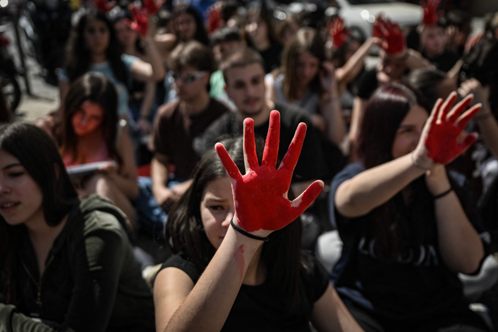 Students from a musical school hold their red painted hands in the air outside a police station during a demonstration against police inaction in feminicides in Athens on April 5, 2024. (Photo by Aris MESSINIS / AFP)
