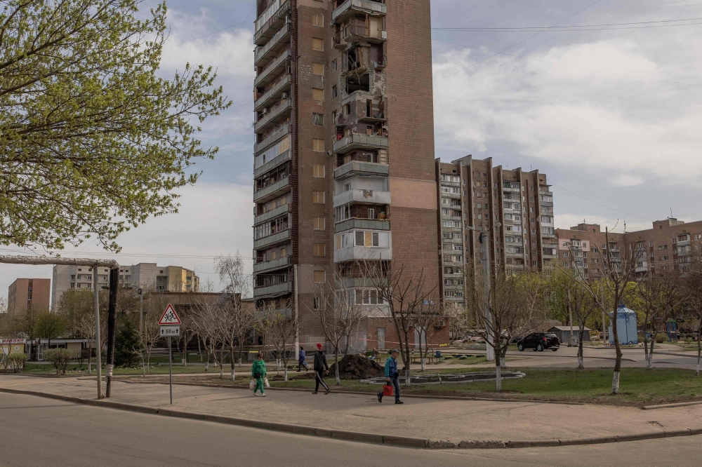 People walk past a residential building that was recently damaged during Russian attacks on the city, in Kharkiv, on April 9, 2024, amid the Russian invasion of Ukraine. (Photo by Roman PILIPEY / AFP)