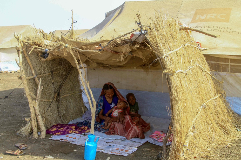 (FILES) A picture taken on March 20, 2024, shows a displaced woman and her children sitting in the shade of a straw hut at a camp in southern Gadaref state for people who fled Khartoum and Jazira states in war-torn Sudan. (Photo by AFP)
