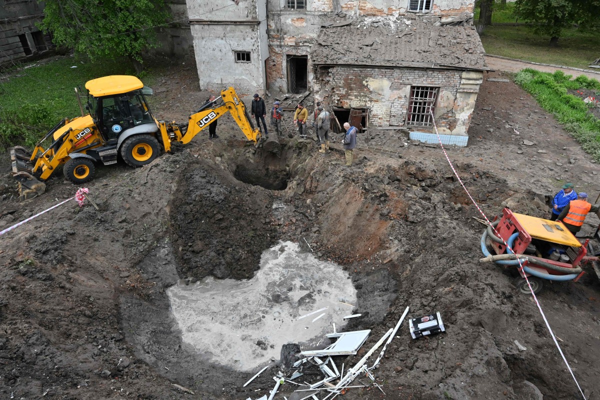 Utility workers operate next to a crater in the courtyard of a hospital in Kharkiv on April 27, 2024, as Russia launched a 