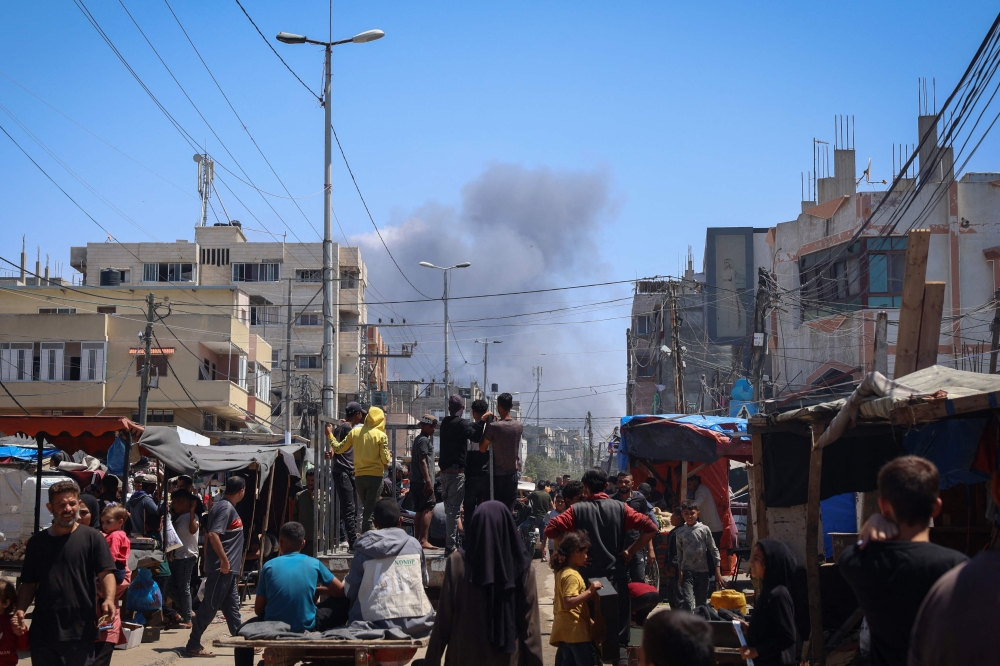 Palestinians crowd a street as smoke billows nearby from Israeli strikes in Rafah in the southern Gaza Strip on May 7, 2024. (Photo by AFP)