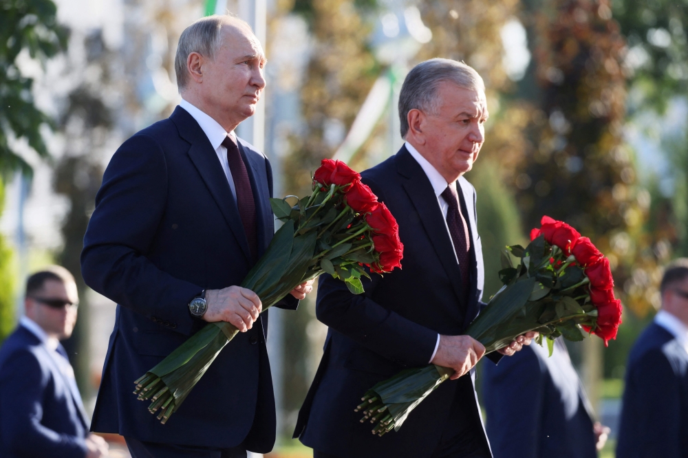 In this pool photograph distributed by the Russian state agency Sputnik, Russia's President Vladimir Putin (left) and Uzbekistan's President Shavkat Mirziyoyev attend a flower laying ceremony at the 