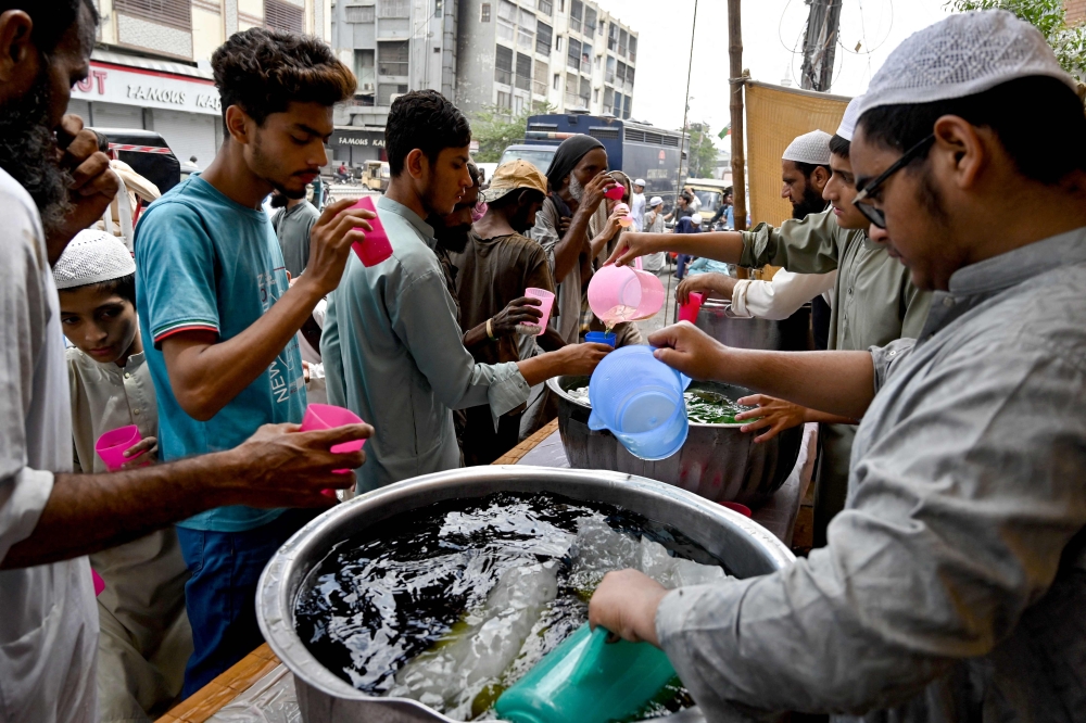Volunteers distribute chilled soft drinks to people at a heatwave relief camp along a roadside on a hot summer afternoon in Karachi on June 3, 2024. (Photo by Asif HASSAN / AFP)