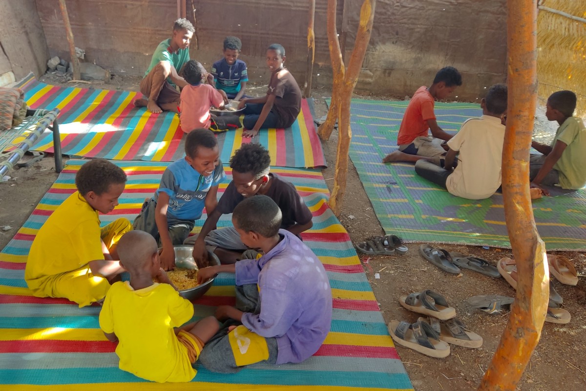 Children sit together sharing a large bowl of food, as Sudanese families host internally displaced people coming from the central Sudanese state of Gezira to the eastern Sudanese city of Gedaref on June 3, 2024. Photo by Ebrahim HAMID / AFP.