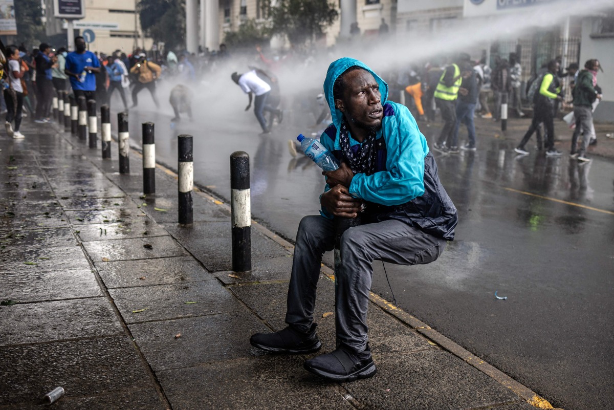 A protester reacts as a Kenyan police water canon sprays water at them during a demonstration against tax hikes as Members of the Parliament vote the Finance Bill 2024 in downtown Nairoibi, on June 20, 2024. (Photo by LUIS TATO / AFP)
 