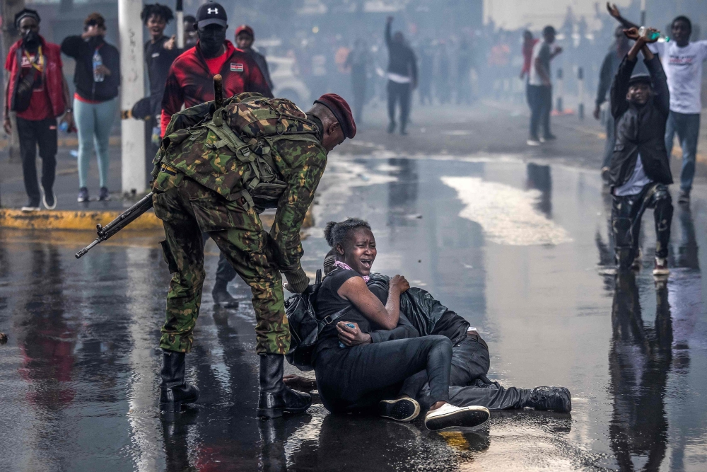A protester cries on the ground while bracing next to another protester after being srpayed by a police water canon truck during a demonstration against tax hikes as Members of the Parliament vote the Finance Bill 2024 in downtown Nairoibi, on June 20, 2024. (Photo by LUIS TATO / AFP)
