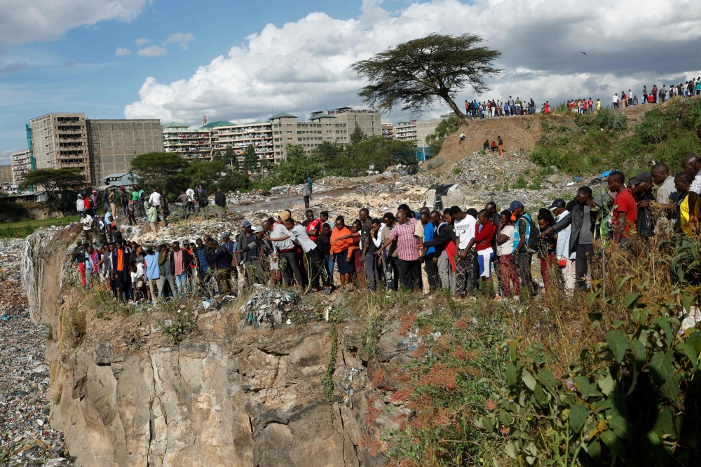 People stand on the edge of a dumpsite where six bodies were found at the landfill in Mukuru slum, Nairobi, on July 12, 2024. Kenyan police have announced the opening of an investigation after the discovery of six bodies in a landfill in the capital Nairobi on Friday. (Photo by SIMON MAINA / AFP)