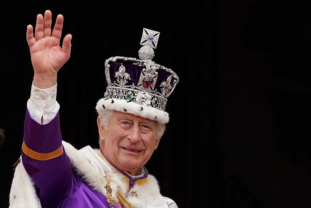 File: Britain's King Charles III wearing the Imperial state Crown, waves from the Buckingham Palace balcony after viewing the Royal Air Force fly-past in central London on May 6, 2023, after his coronation. (Photo by Stefan Rousseau / POOL / AFP)