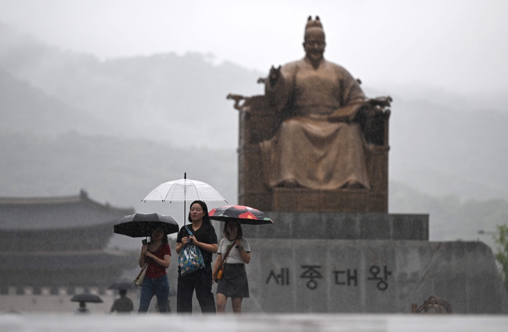 People hold umbrellas as they walk past a statue of King Sejong at the central Gwanghwamun square during rainfall in Seoul on July 18, 2024. (Photo by Jung Yeon-je / AFP)