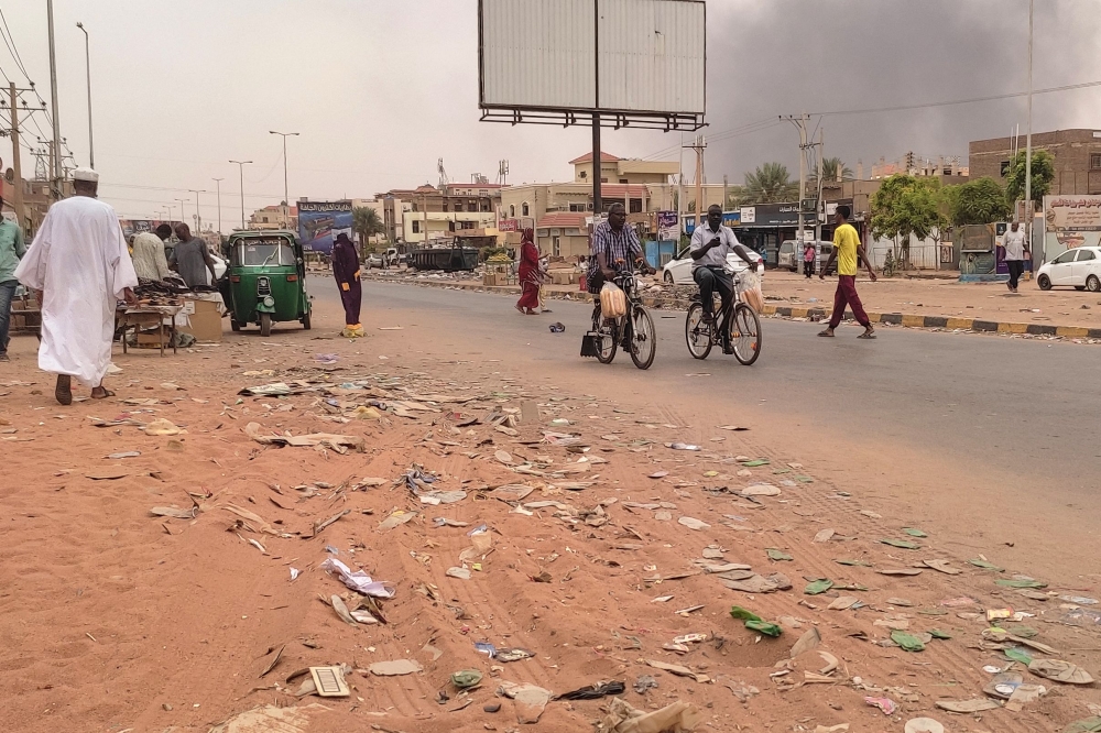 Smoke rises above buildings as people walk along a street in Omdurman City in Sudan on July 15, 2023. (Photo by AFP)


