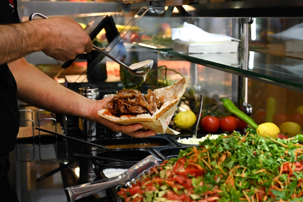 An employee prepares a doner with meat from a kebab skewer in a doner restaurant in the city centre of Dortmund, western Germany on July 26, 2024. (Photo by Ina FASSBENDER / AFP)
