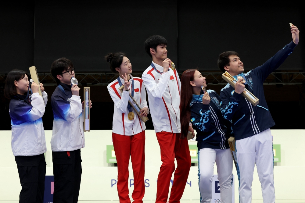 Gold medalists Yuting Huang and Lihao Sheng of Team China (L), Silver medalists Hajun Park and Jihyeon Keum of Team Republic of Korea (L) and Bronze medalists Alexandra Le and Islam Satpayev of Team Kazakhstan (R) take a selfie on the podium during the Shooting medal ceremony on July 27, 2024. (Photo by ALAIN JOCARD / AFP)