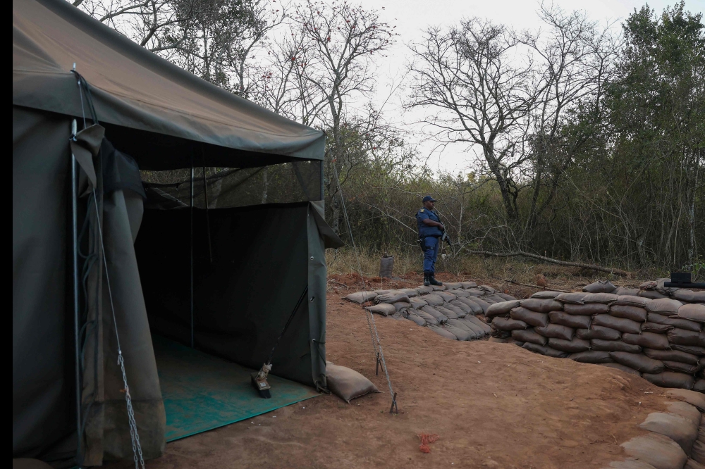 A armed South African Police Services (SAPS) officer stands near the entrance to a farm where they detained ninety five Libyan nationals for receiving training at what authorities suspect to be a secret military camp in White River, Mpumalanga province on July 27, 2024. (Photo by Phill Magakoe / AFP)
