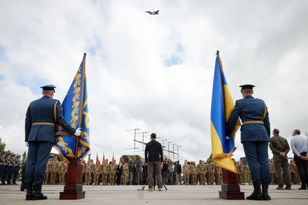 In this handout photograph taken and released by the Ukrainian Presidential Press Service on August 4, 2024, Ukraine's President Volodymyr Zelensky (center) watches a pair of F16 jets flying during Ukraine's Air Force Day celebrations at an undisclosed location. (Photo by Handout / UKRAINIAN PRESIDENTIAL PRESS SERVICE / AFP) 