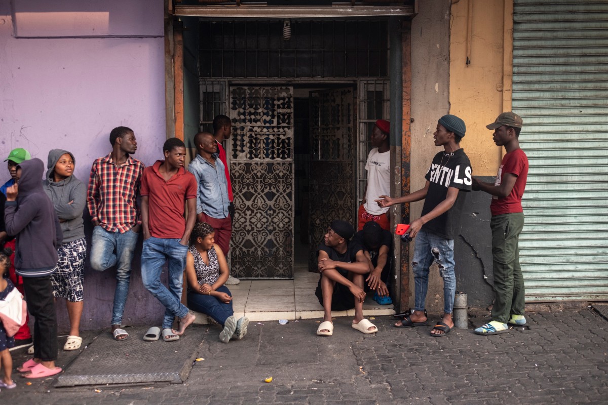 People chat as they gather in the street to watch a building that caught fire in Johannesburg on August 11, 2024. Photo by EMMANUEL CROSET / AFP.