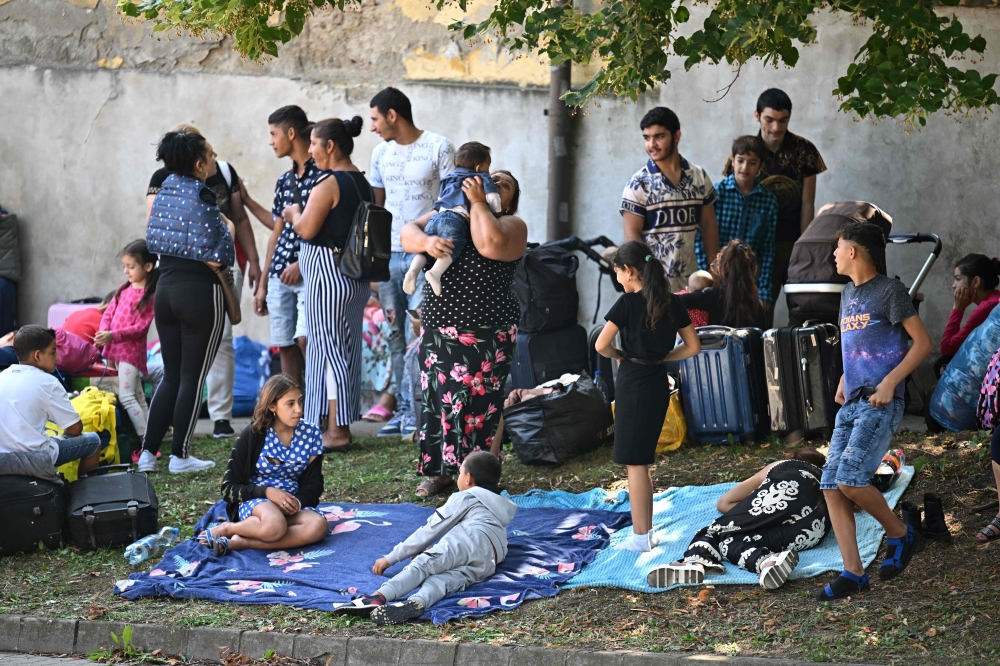 Refugees sit on the pavement close to their former shelter in Kocs village, about 70 km north-west from the Hungarian capital Budapest, on August 21, 2024. (Photo by Attila 
Kisbenedek / AFP)
 