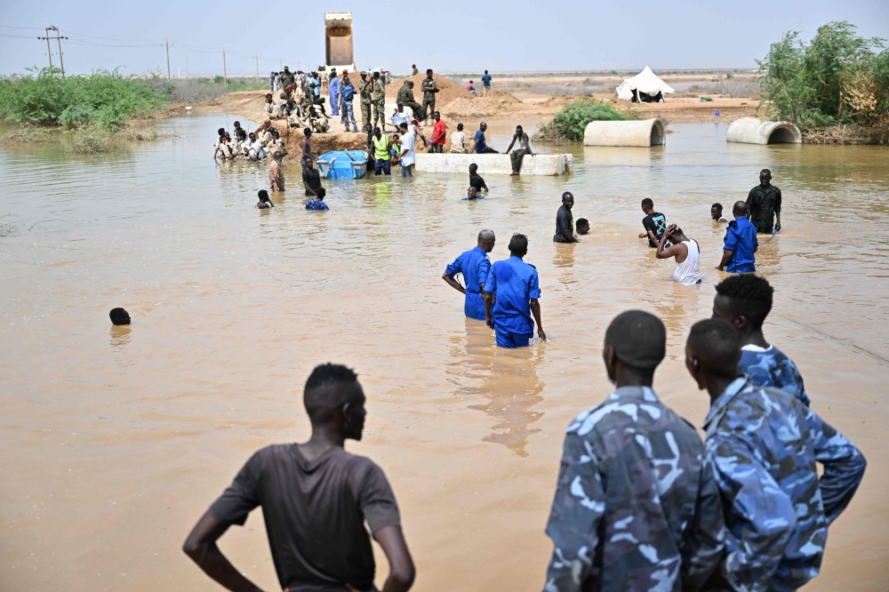Sudanese army soldiers look on as people use a boat in an inundated area in Tokar in the Red Sea State, following recent heavy flooding in eastern Sudan, on September 5, 2024. Photo by AFP