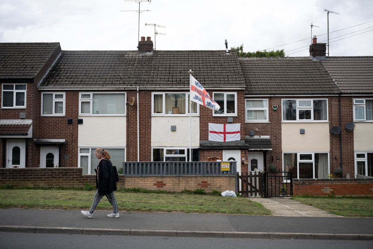 Photo used for demonstration purposes. A woman walks past a house displaying two St George's Cross flags in Leeds, northern England on September 4, 2024. Photo by Oli SCARFF / AFP.