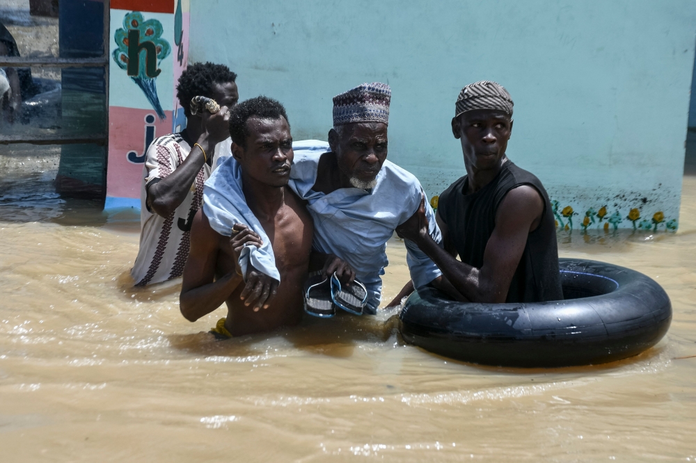 People help an elderly man wade through flood water in Maiduguri on September 12, 2024.  (Photo by Audu Marte / AFP)

