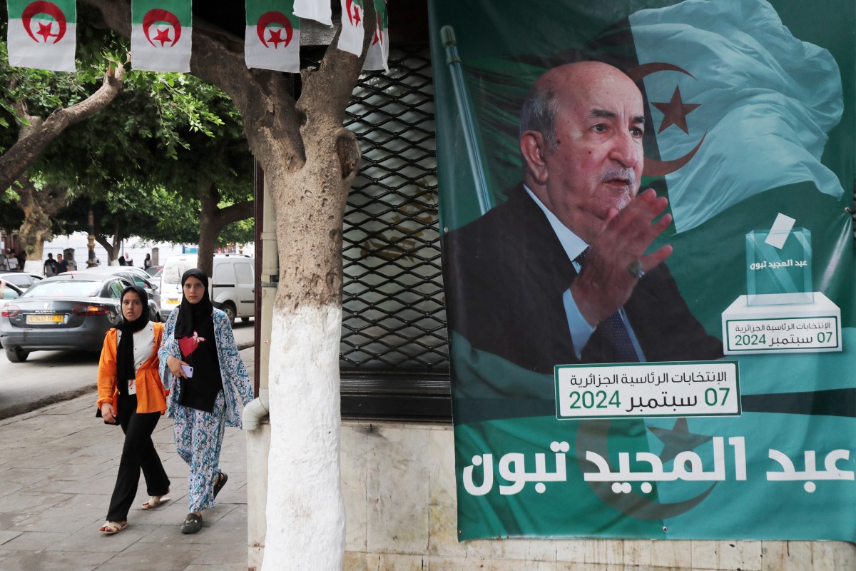 People walk past posters of Algeria's President Abdelmajid Tebboune outside an election campaign headquarters in Algiers on September 8, 2024. Photo by AFP.