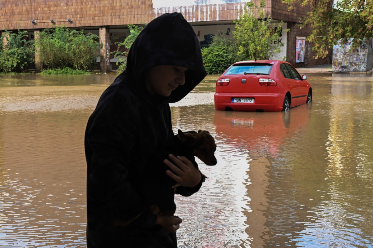 A boy holding a dog walks besides a street flooded by the Opava river on September 15, 2024 in Opava, Czech Republic. (Photo by Michal Cizek / AFP)
