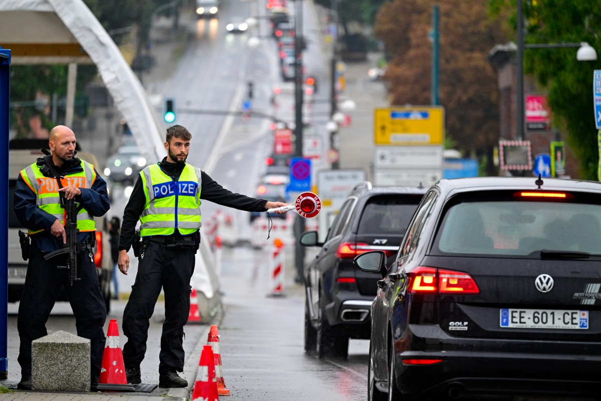 A German police officer flags down a car while controlling the traffic flow from Poland across the 