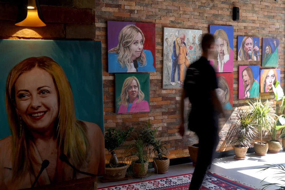 A customer walks past portrait paintings of Italy's Prime Minister Giorgia Meloni adorning the wall of 