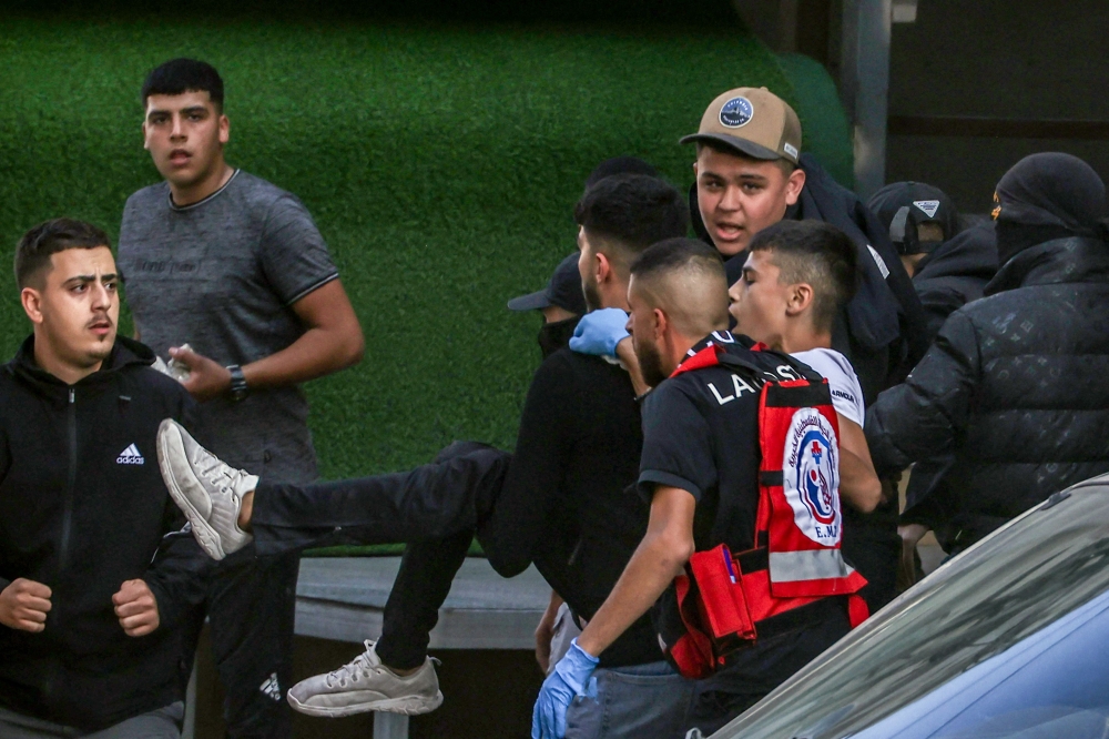 People carry an injured man during clashes between Palestinian youths and Israeli forces as the army conducts a military raid in Kafr Aqab east of Ramallah in the occupied West Bank on October 7, 2024. (Photo by Zain JAAFAR / AFP)
