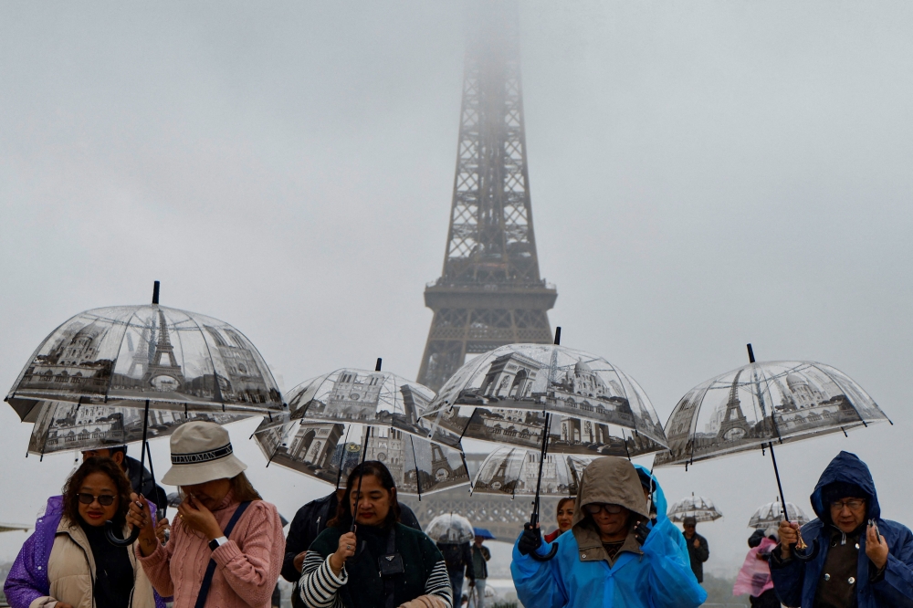 Visitors shelter from the rain with umbrellas on the Parvis des Droits de l'Homme on Esplanade du Tocadero across from the Eiffel Tower, as remnants of hurricane Kirk cause heavy rainfall over Paris, on October 9, 2024. (Photo by Ludovic MARIN / AFP)
