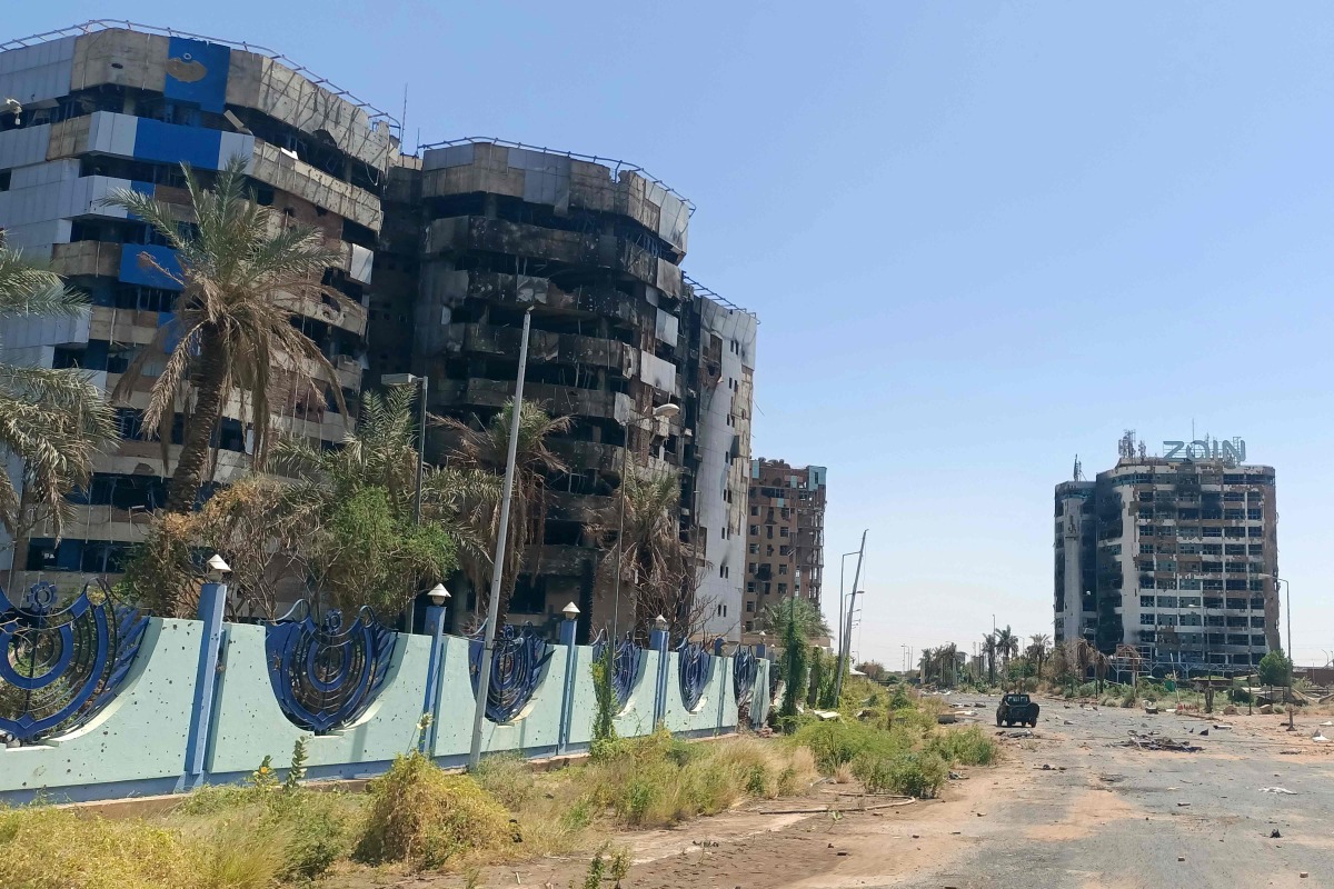 A vehicle moves along a road past (L) the heavily damaged building that housed the headquarters of the Central Bank of Sudan is pictured in Khartoum's Muqrin neighbourhood on March 22, 2025. (Photo by AFP)
