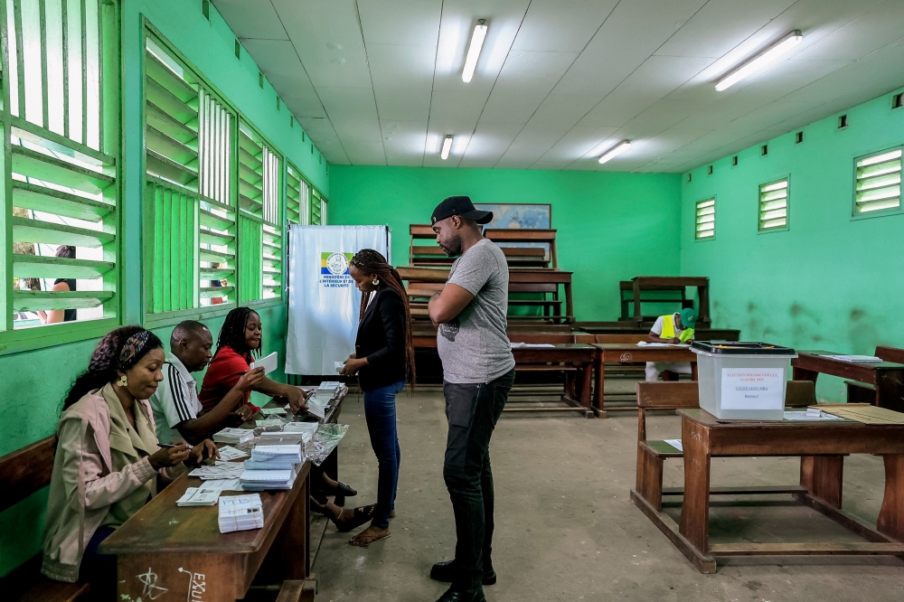 Voters receive their ballot papers from electoral officials at the Lycee Leon Mba polling station in Libreville on April 12, 2025 during Gabon's presidential election. (Photo by Daniel Beloumou Olomo / AFP)